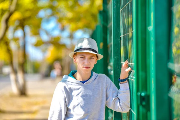 Vzteklý a nespokojený chlap v klobouku se drží zeleného plotu a dívá se do kamery. — Stock fotografie