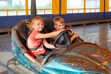 Çocuklar lunaparkta elektrikli arabalara biniyorlar..