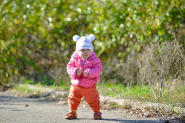 Küçük bir çocuk sonbaharda ve bahar kıyafetleri içinde parkta yürür..
