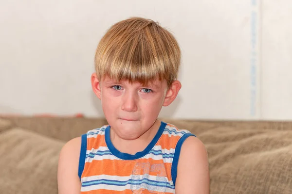 En ledsen och ledsen pojke sitter och gråter på soffan. — Stockfoto