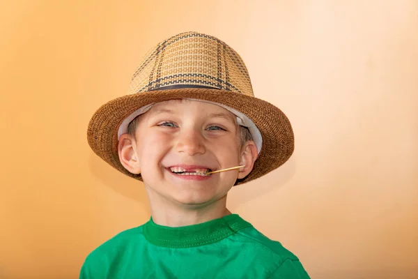 Um menino de chapéu de palha com um palito nos dentes sorri e eis — Fotografia de Stock