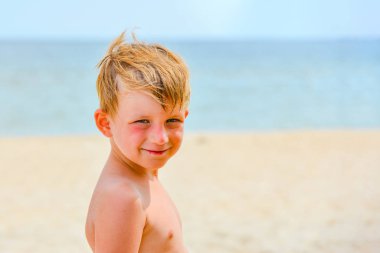 Denizin arka planında bir çocuk ve mavi gökyüzü sahilde duruyor ve gülümsüyor..