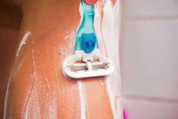 Chica se afeita las piernas con una navaja de afeitar, extendiendo espuma sobre ellos —  Fotos de Stock