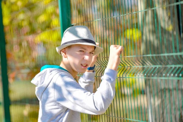 Ritratto di un giovane malvagio con un cappello vicino a una recinzione verde . — Foto Stock