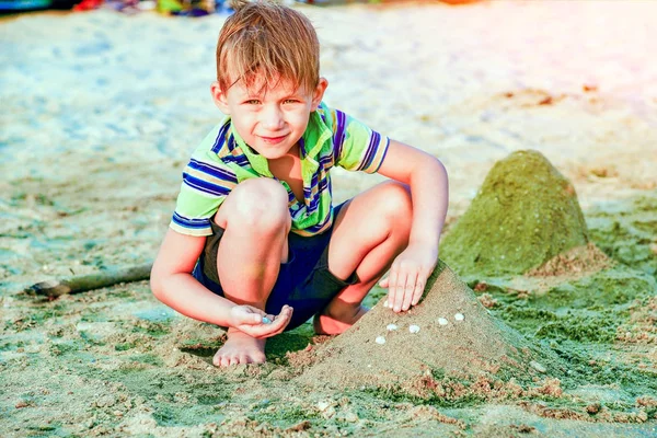 A boy at the sea plays in the sand and builds sand castles on the beach. — ストック写真