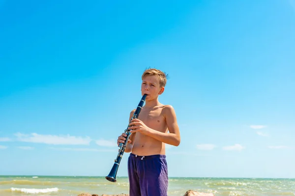 Un garçon joue avec la clarinette sur la plage au bord de la mer . — Photo