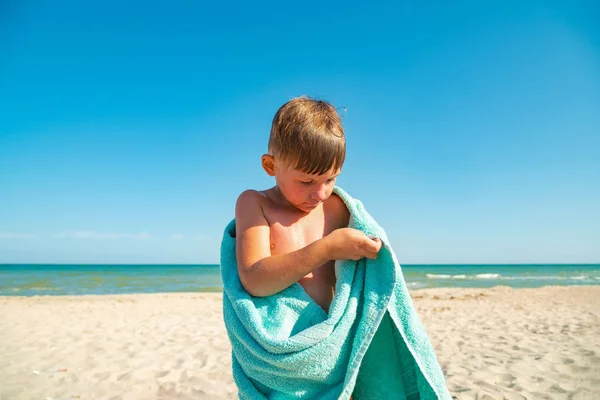 Il ragazzo sulla spiaggia si nasconde con un asciugamano e si asciuga dall'acqua di mare dopo aver nuotato nel mare. . — Foto Stock