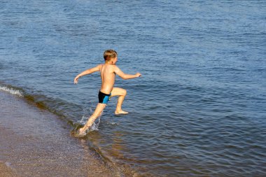 Neşeli ve mutlu çocuk deniz sahilinde koşuyor..