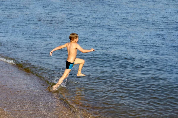 Radosny i szczęśliwy chłopiec biega po wodzie na plaży morskiej. — Zdjęcie stockowe