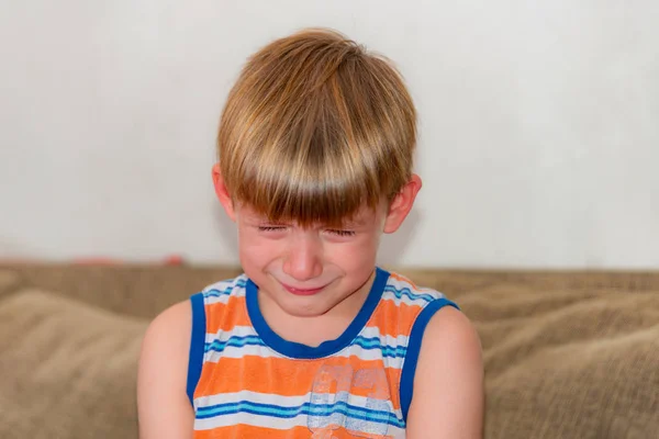 Smutny i smutny chłopiec siedzi i płacze na kanapie. — Zdjęcie stockowe