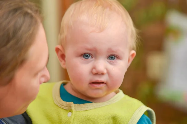 Un petit enfant s'assoit dans les bras de sa mère et pleure les larmes aux yeux . — Photo