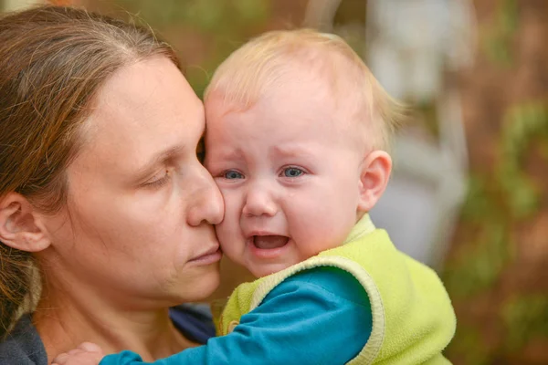 Un bambino piccolo siede tra le braccia della madre e piange con le lacrime agli occhi . — Foto Stock