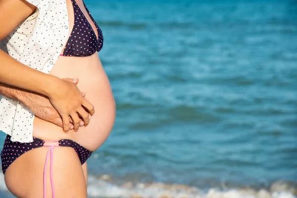 Un uomo tiene la pancia di una donna incinta su uno sfondo del mare . — Foto Stock