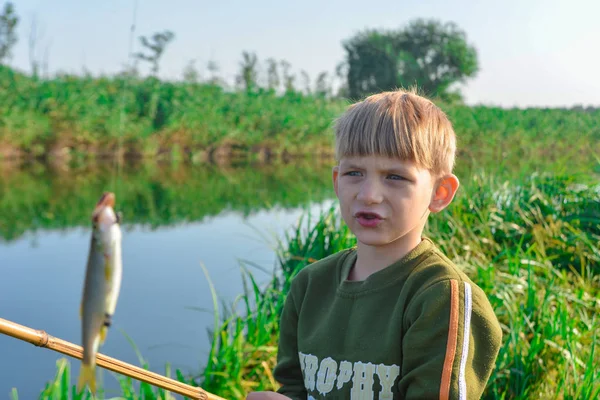 Радостный и удивленный мальчик держит рыбу висящую на удочке . — стоковое фото