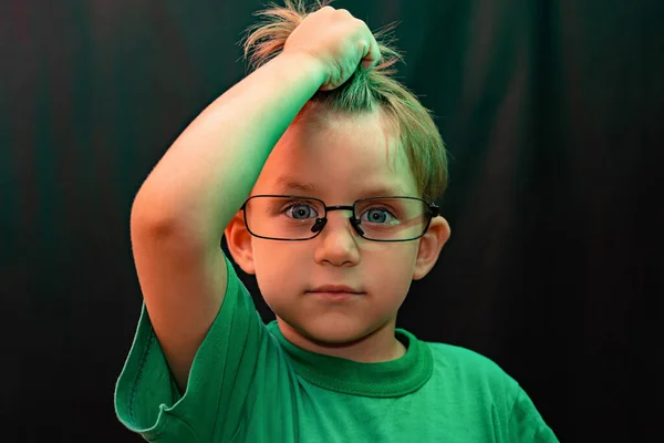 Niño sorprendido en gafas sobre un fondo negro sostiene su mano con su pelo y mira hacia arriba —  Fotos de Stock