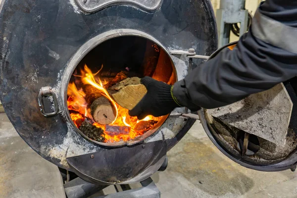 Arbeiter wirft Brennholz in einen Ofen, um einen Raum zu heizen. — Stockfoto