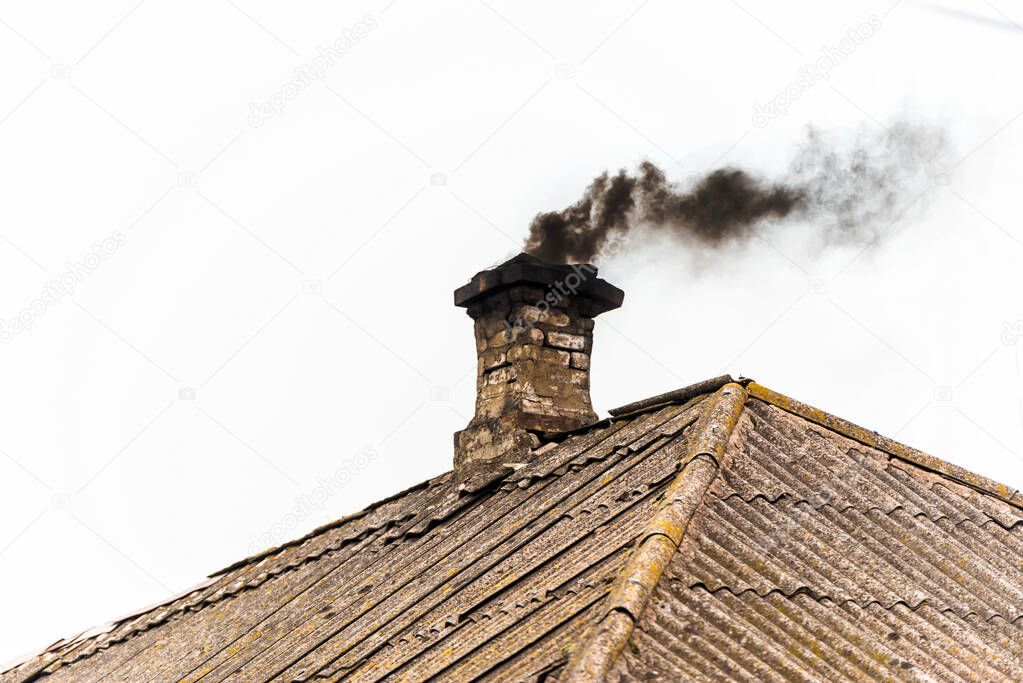 Black smoke from the chimney of an apartment building during heating and heating on the roof of slate.