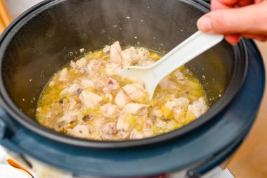 Kadın tencerede beyaz bir kaşıkla yahniyi karıştırıyor..