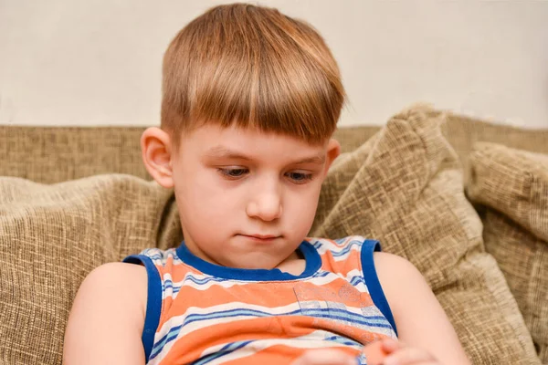 Un chico triste se sienta en el sofá y mira hacia abajo . — Foto de Stock