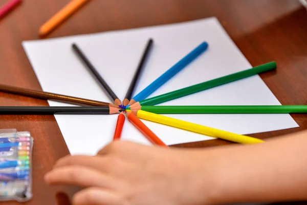 Color pencils lie on a blank white sheet on the table.