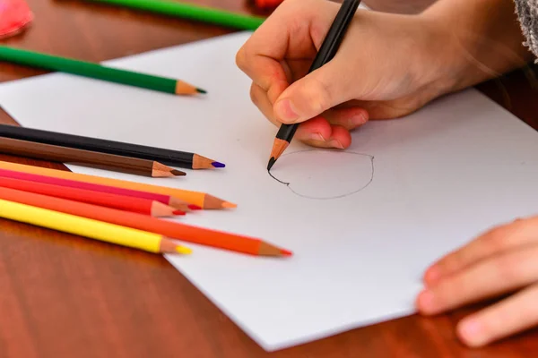 A girl draws a heart with colored pencils on a white sheet among children's toys. — 스톡 사진