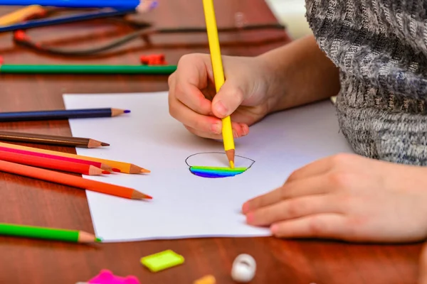 Ένα κορίτσι ζωγραφίζει μια καρδιά με χρωματιστά μολύβια σε ένα λευκό φύλλο ανάμεσα στα παιδικά παιχνίδια. — Φωτογραφία Αρχείου