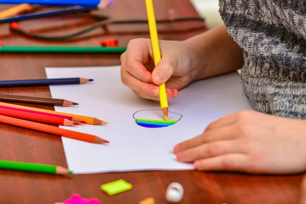 A girl draws a heart with colored pencils on a white sheet among children's toys. — 스톡 사진