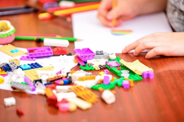 Una chica dibuja un corazón con lápices de colores en una sábana blanca entre los juguetes de los niños . — Foto de Stock