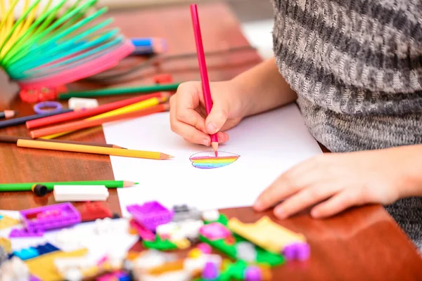 A girl draws a heart with colored pencils on a white sheet among children's toys. — 스톡 사진