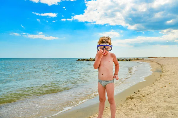 Um menino com óculos para mergulho fica na praia. . — Fotografia de Stock