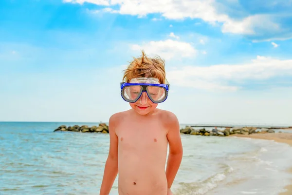 En pojke med glasögon för dykning står på stranden. — Stockfoto