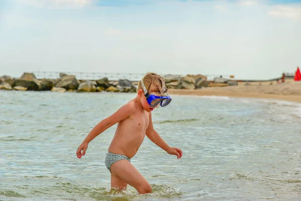 En pojke med glasögon för dykning står på stranden. — Stockfoto