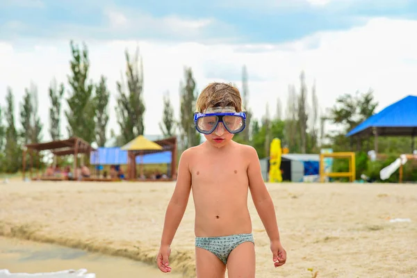 Um menino com óculos para mergulho fica na praia. . — Fotografia de Stock