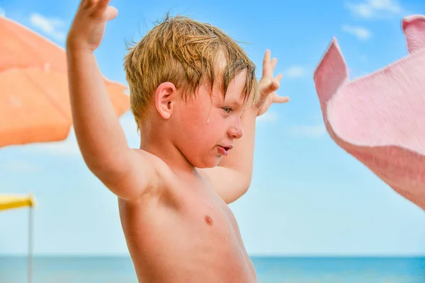 Chłopiec nad morzem na plaży wśród parasoli przeciwsłonecznych wyciągnął ręce na boki. — Zdjęcie stockowe
