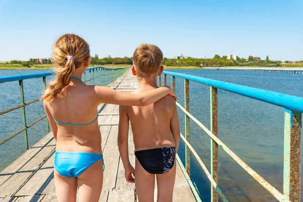 Brother and sister are hugging on a bridge across the water. — Stock Photo, Image