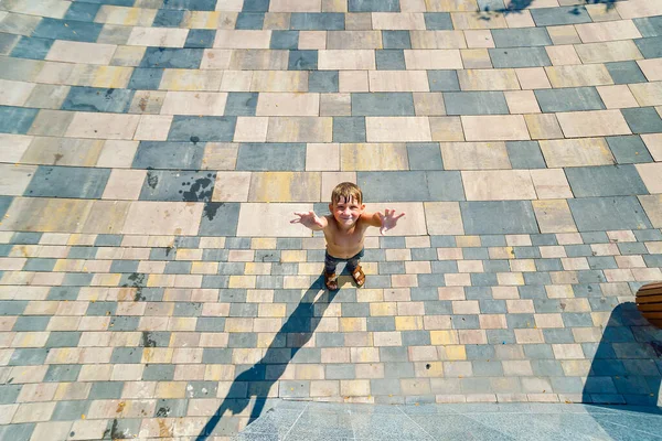 Un niño se para abajo y mira hacia arriba con las manos en alto, vista desde arriba . — Foto de Stock