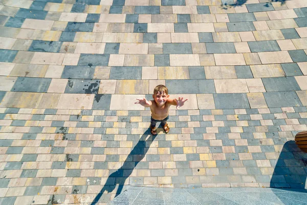 A boy stands below and looks up with his hands up, view from above. — Stock Photo, Image