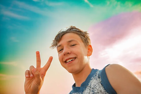 Pojken visar ett tecken V, ett Victoria tecken från en man mot en flerfärgad himmel. — Stockfoto