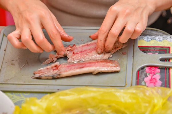 Женщина домохозяйка чистит сельдь, чтобы приготовить рыбную еду — стоковое фото