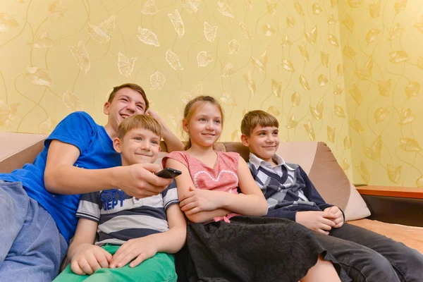 Щасливі та радісні діти сидять на дивані у вітальні. Хлопчик перемикає канали на пульт дистанційного керування телевізора — стокове фото