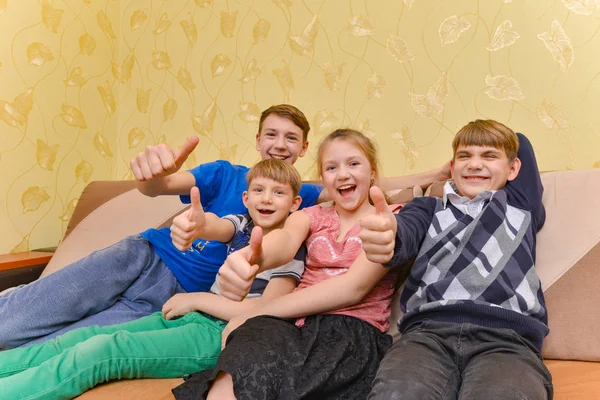 Šťastné a radostné děti sedí na gauči a ukazují palec nahoru — Stock fotografie