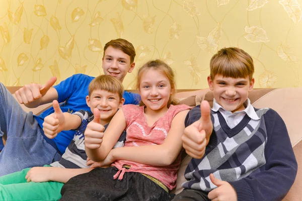 Щасливі і радісні діти сидять на дивані і показують великий палець вгору — стокове фото