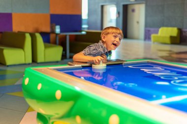 Çocuk, çocuk eğlence merkezinde hava hokeyi oynayarak kazandığı için gülüyor ve seviniyor..