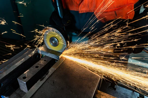 Um trabalhador corta uma peça de trabalho com um moedor, faíscas voam em lados opostos . — Fotografia de Stock