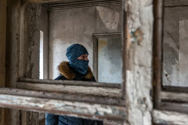 Un adolescente mira por la ventana en una casa abandonada y arruinada . —  Fotos de Stock