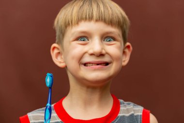 Gülümseyen ve neşeli bir çocuk elinde bir diş fırçası tutuyor..