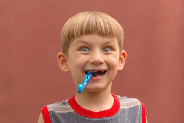 Ağzında diş fırçası olan neşeli çocuk kameraya bakıyor..