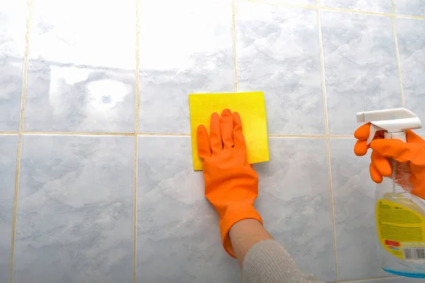 Женщина вытирает плитку в защитных перчатках в ванной комнате с моющим средством . — стоковое фото