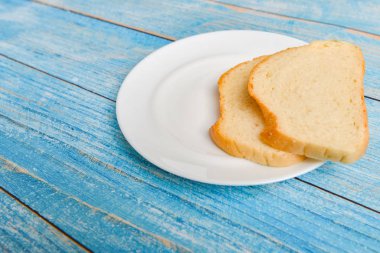 Dilimlenmiş beyaz ekmek beyaz bir tabakta, beyaz ahşap bir arka planda yatıyor..