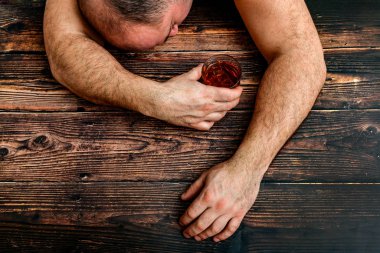 Elinde bir bardak alkol olan sarhoş bir adam ahşap bir masada yatıyor. Alkolizm ve alkol bağımlılığı kavramı.